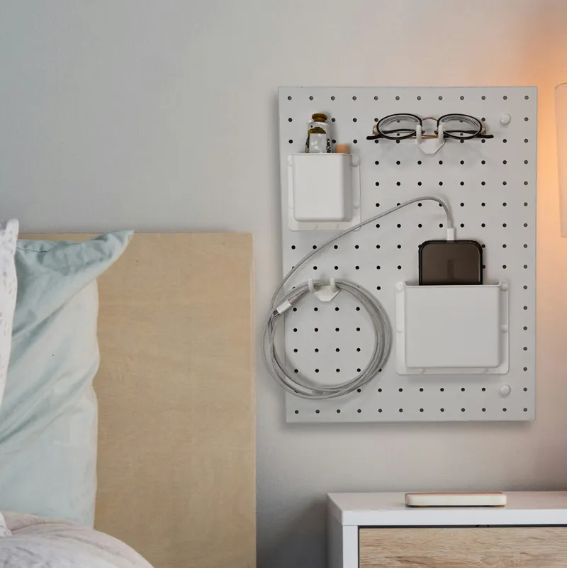 Modular pegboard wall organizer with hooks and bins for bedside wall storage, organizing glasses, cables, and small essentials in a modern home.
